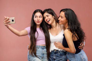 Telefonlarıyla selfie çekerken gülümseyen üç muhteşem kadın.