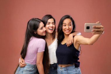 Neşeli yüz ifadeleri olan ve telefonlarına selfie çeken üç zeki arkadaşın stok görüntüsü.