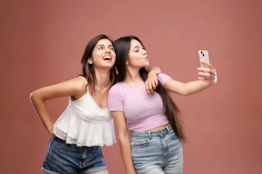 Gündelik kıyafetler giyen iki en iyi arkadaş selfie çekerken pembe bir arkaplan önünde poz veriyorlar.