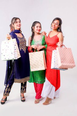 Alışveriş torbalarıyla kameraya bakan Hintli kadınların stüdyo çekimi.