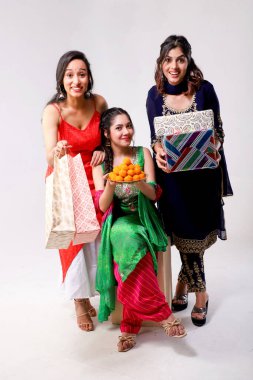 Kameranın önünde poz veren güzel kadın modeller, bir laddu tabağı, hediyeler ve alışveriş poşetleri tutuyorlar. Diwali festivali ve Hint festivali konsepti