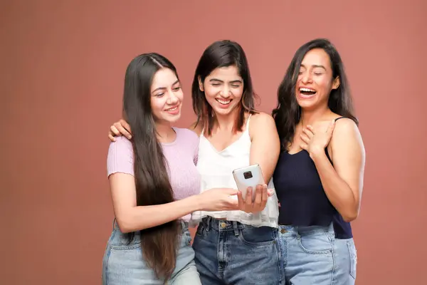 Üç mutlu gülen arkadaş telefonda eğlendirici şeyler izlerken gülüyorlar.