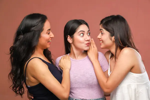 Üç şaşırmış kadın birbirlerine bakarken birbirlerine sarılıp şaşırmış yüz ifadeleri takınıyorlar.