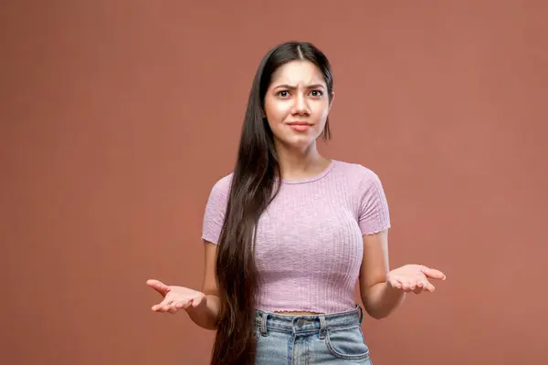 Pembe bir arka planda dikilirken kafası karışmış yüz ifadeleri veren cahil bir kız.