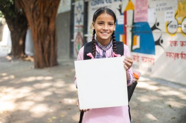 Okulun önünde elinde beyaz bir tahtayla duran liseli kız.