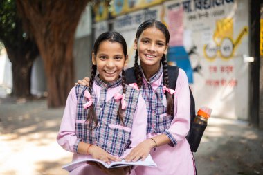 Hindistan köyü öğrencileri ellerinde kitap tutarken okulun önünde gülümsüyor.