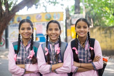 Okul üniformalı üç öğrenci çapraz kollarla duruyorlar.