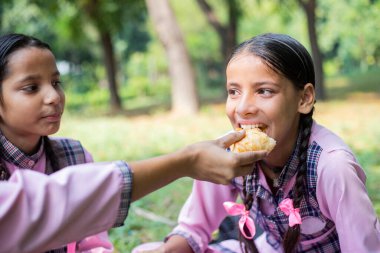 Okul üniformalı bir kız arkadaşının elinden yemek yiyor.