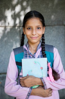 Okul üniformalı mutlu öğrenci elinde çanta ve elinde kitapla kamera önünde poz veriyor. Eğitim kavramı. 