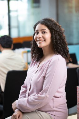 Kadın ofis çalışanı boş boş oturuyor ve gülümsüyor.