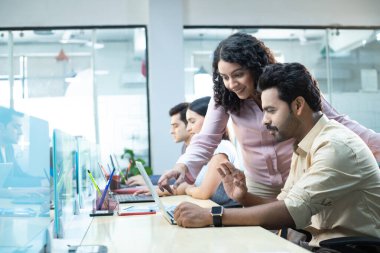 Ekip ofisinde çalışıyor ve erkek meslektaşı iş raporunu görmek için iyi bir jest yapıyor.