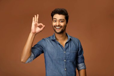 Seksi bir genç adam gülümsüyor ve poz verirken el hareketi yapıyor.