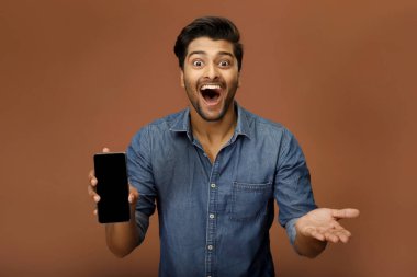 Heyecanlı, genç, zinde bir adam kameraya doğru akıllı telefon ekranını gösteriyor.