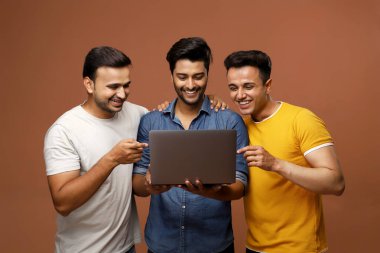 Kameranın önünde poz verirken üç kişi dizüstü bilgisayar kullanıyor.