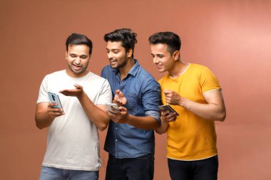 Üç adam kameranın önünde durup sosyal ağ sitelerine bakarken cep telefonlarını kullanıyor.