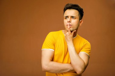 Asyalı bir erkek model parmağını dudaklarına koyarken bir şey düşünüyor.