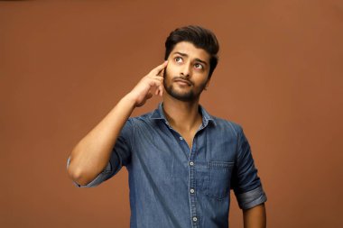 Genç bir erkek model parmağını kafasına koyarken bir şey düşünüyor.