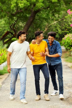 Üç neşeli arkadaş parkta yürürken ve eğlenirken birlikte gülüyorlar.
