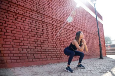 Spor elbiseli kız Sumo Squat egzersizi yapıyor.