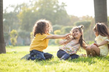 Çimenlerde oturan çocuklar birbirlerini gıdıklarlar. 