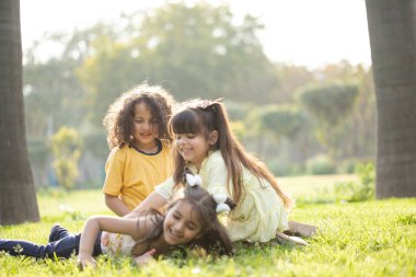 Bahçedeki yeşil çimlerin üzerinde oturan arkadaşlar gülüp oynuyorlar.