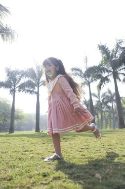  Güneşli bir yaz gününde çimenlerde koşan kız gülümsüyor.