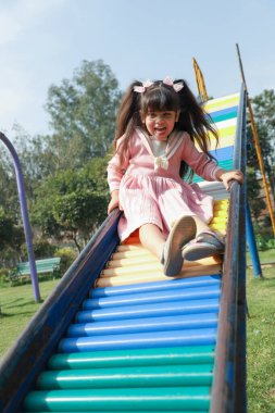 Bir kız parkta oynuyor sürgülü kayıyor ve dışarıda eğleniyor.