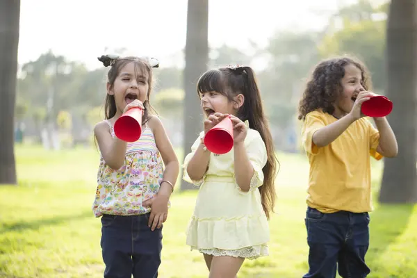 Yaramaz çocuklar parkta dikilip kırmızı kağıt megafona bağırıyorlar.