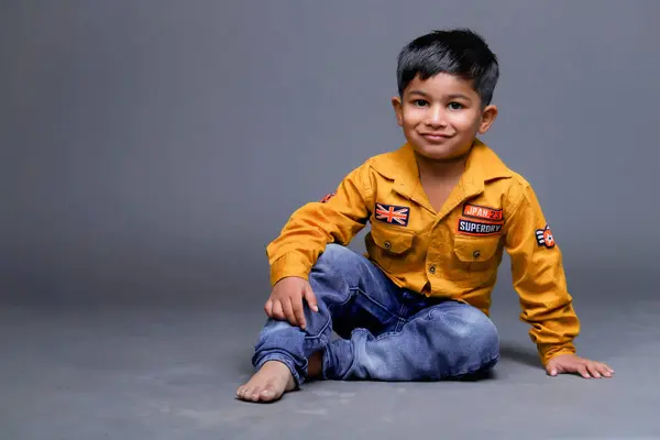 Yerde kot pantolon ve gömlek giyen mutlu bir çocuğun portresi duruyor.