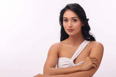 Kendine güvenen ve kendine güvenen bir kadın beyaz bir arkaplan karşısında zarafetle oturur..