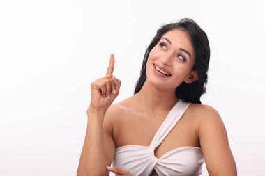 Beyaz bluzlu güzel bir Asyalı kadın, temiz bir arkaplan ile parmaklarını yukarı kaldırarak, çekiciliğini ve pozitifliğini gösterir..