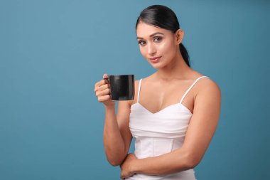 Bir Moda Modeli minimalist bir stüdyoda elinde bir fincan kahve tutarken zarif bir poz verir..