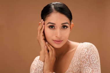 Çekici genç bir kadın, kahverengi bir stüdyo geçmişine karşı özgüvenle poz verir. Zarafet ve cazibe yayar..