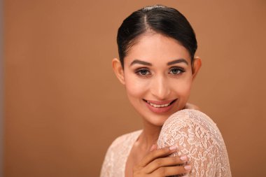 Model, doğal güzelliğini ve özgüvenini vurgulayarak tarafsız bir zemine karşı sıcak bir gülümsemeyle zarifçe poz verir..