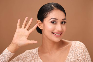 Bir kadın sıcak, kahverengi bir arkaplanda zarif bir şekilde poz verir ve elini kaldırarak beş numarayı gösterir..