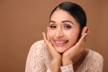 Sevimli bir kadın neşeli ve sevimli bir poz verir, iki elini de nazikçe çenesinin altına koyar..