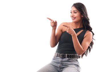 Genç bir Asyalı kız beyaz bir bankta oturuyor, ilginç bir şekilde sola bakarken yan tarafa bakıyor..