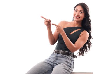 Genç bir kız boş bir reklam panosunda oturuyor, kendine güvenerek farklı bir yöne bakıyor ve gülümsüyor..