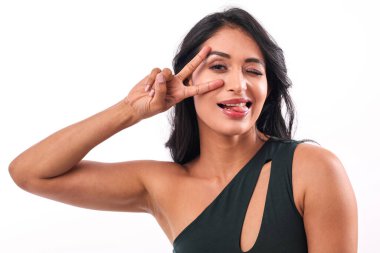 Genç bir bayan beyaz bir arka plana karşı poz veriyor, neşeli bir ifadeyle gözlerinin yanında bir V işareti yapıyor. Eğlence, moda ve anlamlı yaşam tarzı kavramları için mükemmel..