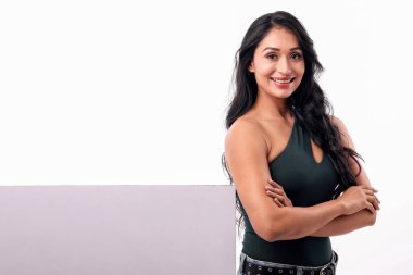 Uzun siyah saçları ve sıcak bir gülümsemesi olan özgüvenli ve dengeli bir kadın boş bir pankartın yanında kollarını kavuşturur. bu resim promosyon veya reklam içeriği için idealdir.