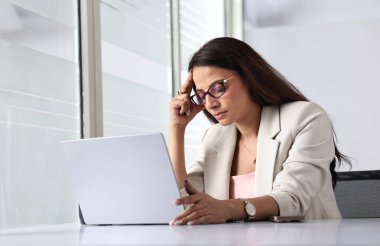 Modern ofis ortamında dizüstü bilgisayarında yazan derin düşüncelere dalmış bir kadın..