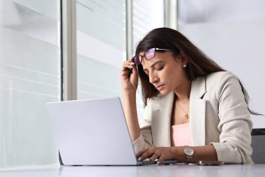 Bir kadın, parlak bir ofisteki dizüstü bilgisayardaki işine konsantre oluyor..