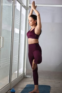 Bir kadın, iyi aydınlatılmış bir stüdyoda yoga pozu verirken tek bacağının üzerinde dengede durur..