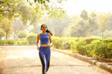 Parkta koşan, rahat spor kıyafetleri giyen ve açık havada koşmaktan zevk alan bir kadın..