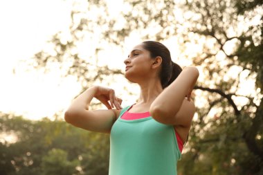Genç bir kadın parkta dinlenmek için yoga yapıyor. Huzurlu bir ifadeyle nazik bir duruş sergiliyor..