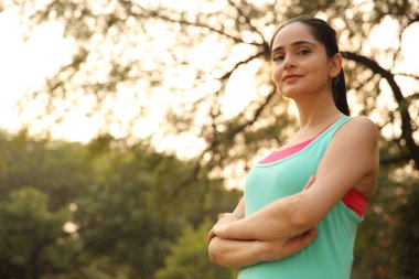 Güçlü, bağımsız bir kadın kollarını kavuşturmuş, parlak bir şekilde gülümsüyor ve rahatlatıcı, doğal bir ortamda kendine güven ve pozitiflik yayıyor..