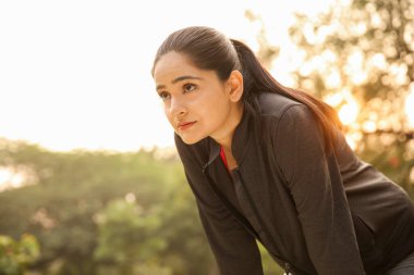Bir kadın parkta koştuktan sonra dinleniyor, soluklanıyor ve huzurlu ortamın tadını çıkarıyor..