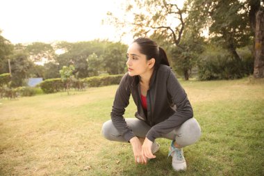 Siyah ceketli bir kadın parkta koşuyor, dinleniyor ve dinleniyor. Açık havada huzurlu bir şekilde soluklanıyor..
