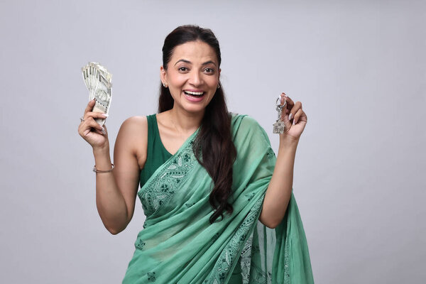 Улыбающаяся женщина держит деньги в одной руке, а ключи в другой, надевая красочный традиционный наряд.