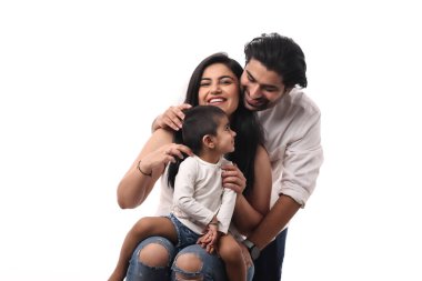 Genç bir çift, neşeli çocuklarını parlak bir mekanda tutarken sarılır ve gülümser..